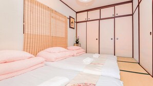 Un lit bien fait, agrémenté de serviettes roses et blanches, un plancher en bois et, au fond, une porte coulissante traditionnelle japonaise.