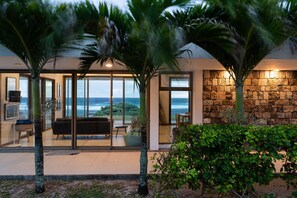 Una casa moderna con puerta de cristal que da a un salón con vistas al océano.