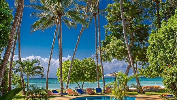 A pool area with palm trees, lounge chairs, and a view of the ocean. - Monkey Beach House, Beachfront, Ocean Views,  Shared Pool, Staff Provided (Diani Beach)