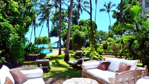 A tropical outdoor lounge area with a pool, lounge chairs, and a wooden table. - Monkey Beach House, Beachfront, Ocean Views,  Shared Pool, Staff Provided (Diani Beach)