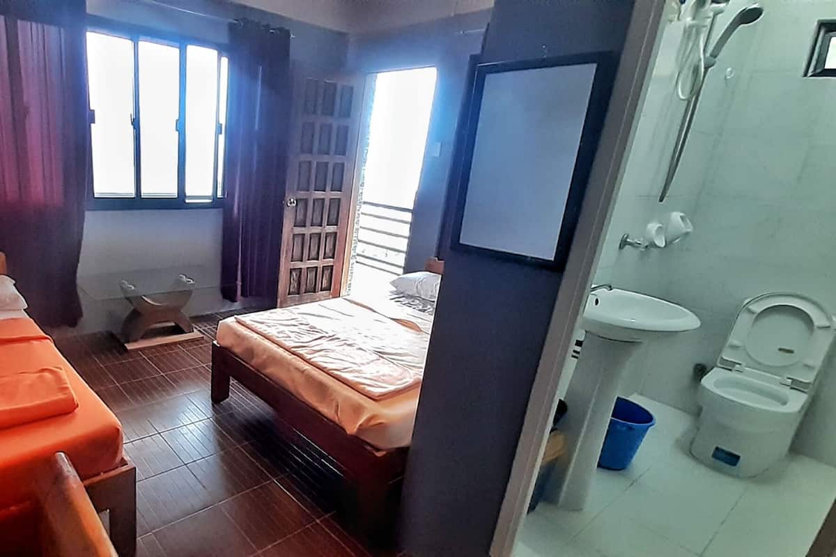Ein Zimmer mit zwei Betten, einem Fenster mit Vorhängen, einem kleinen Tisch und einem Badezimmer mit Waschbecken und Toilette.