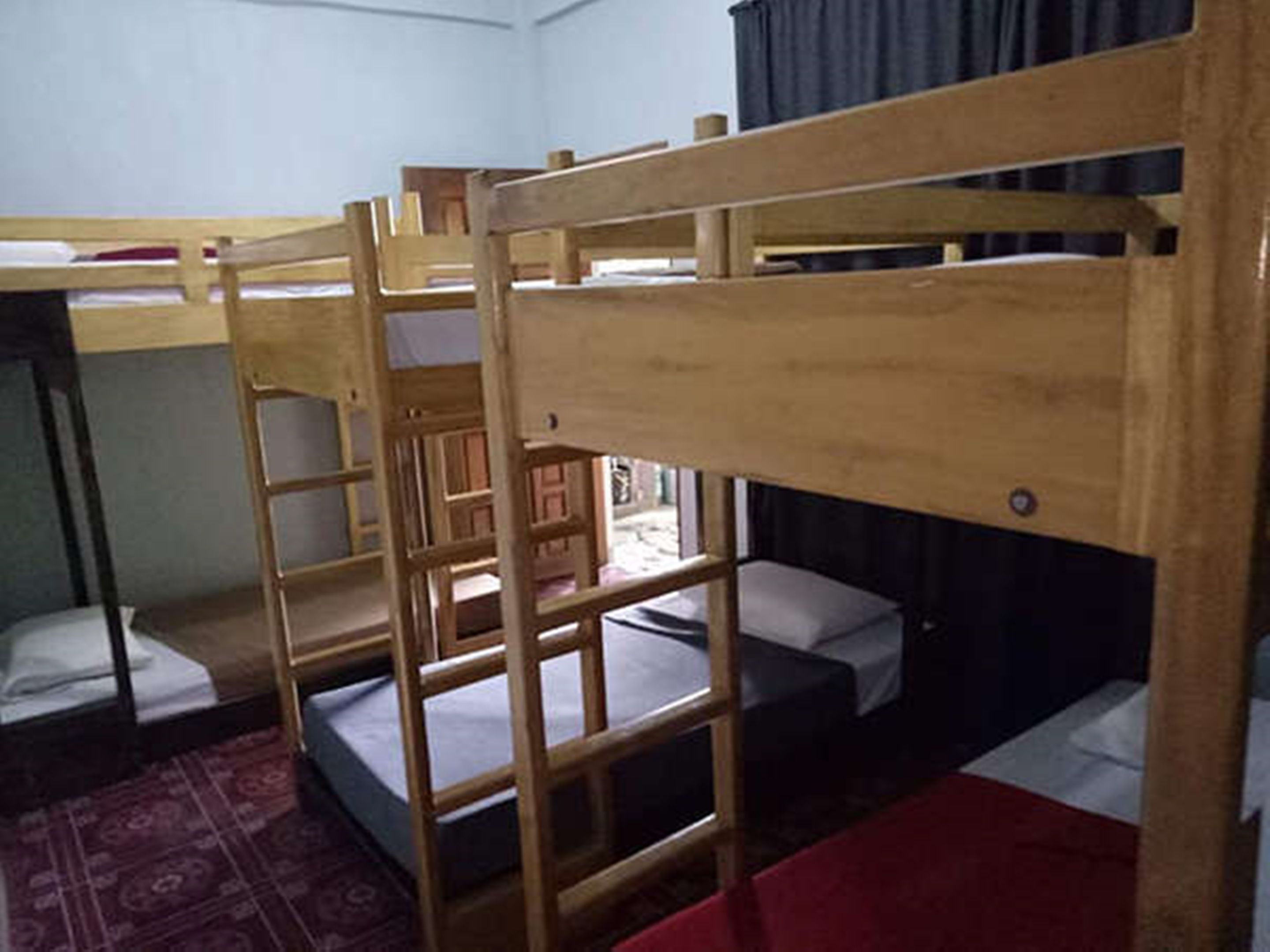 Habitación con literas, alfombra roja, muebles de madera y una ventana con cortinas.