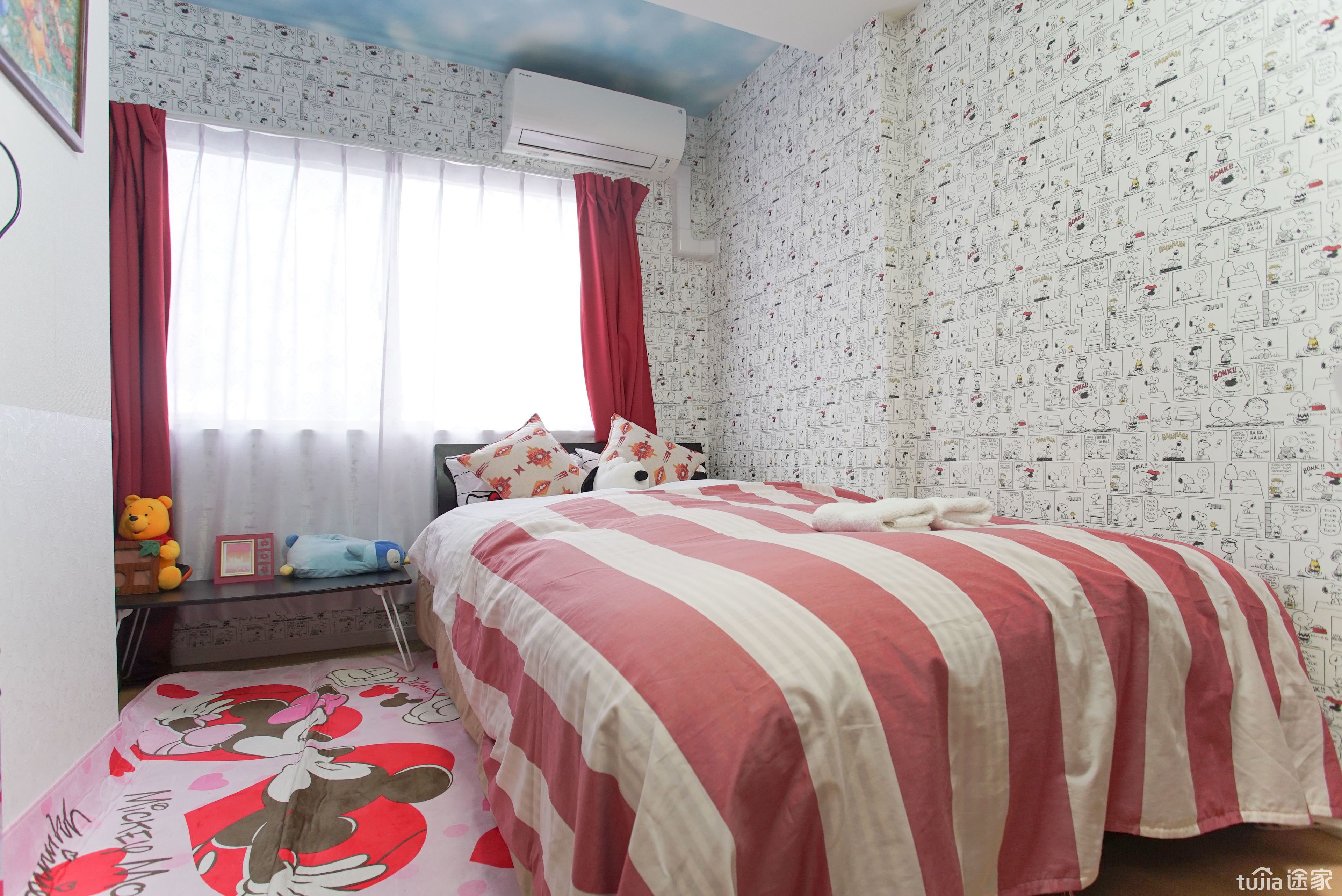 Een slaapkamer met een gestreepte sprei, vloer met Mickey Mouse thema en een raam met rode gordijnen.