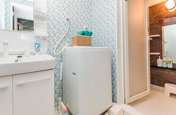 A bathroom with a white sink, a white washing machine, a blue and white tiled wall, and a wooden door.