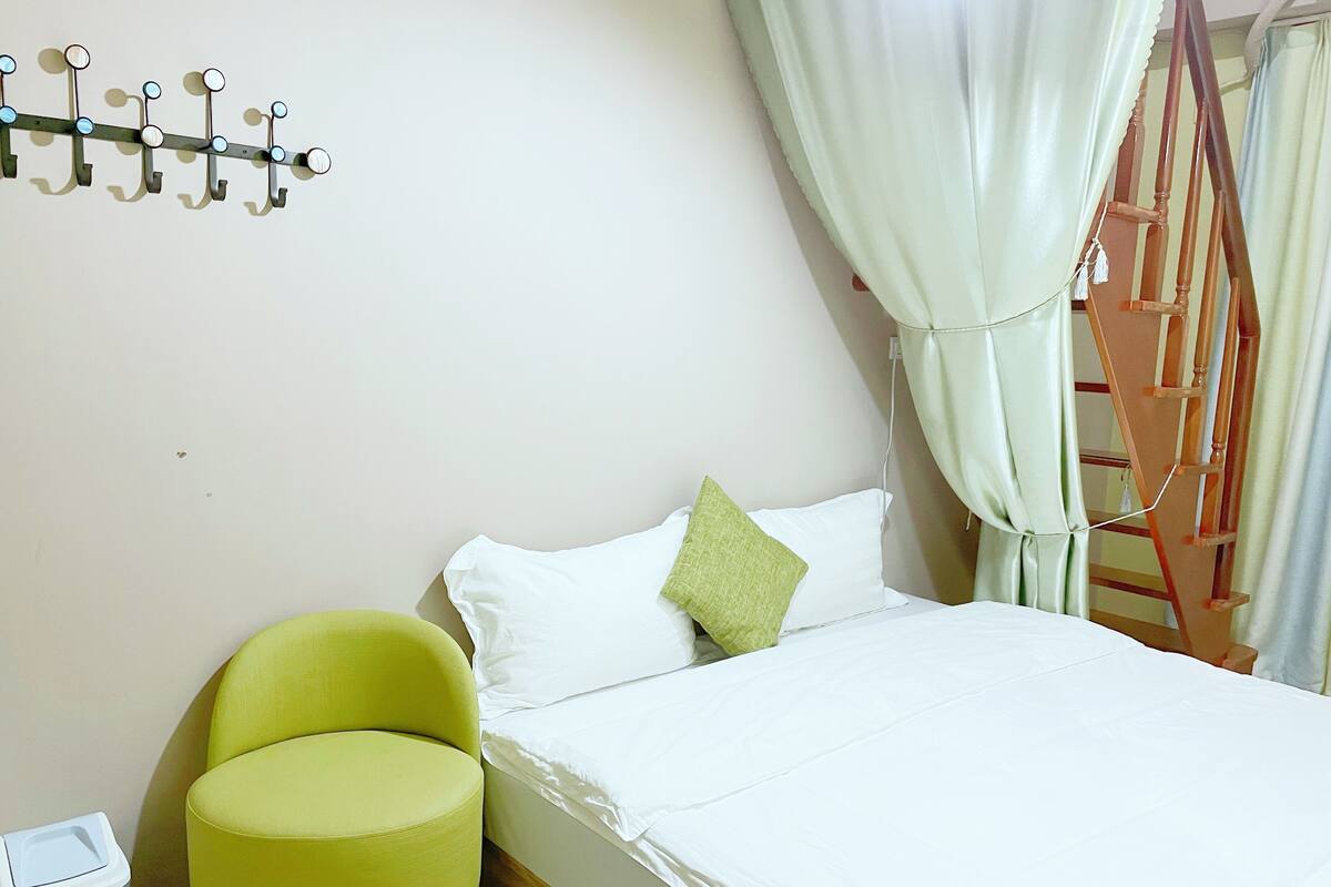 A bedroom with a bed, a chair, a wall-mounted hookboard, a curtain, and a staircase.