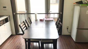 A kitchen with a dining table, chairs, a refrigerator, and a window with a view. - Osaka Sinsei Guest House (Osaka)