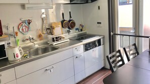 A modern kitchen with white cabinets, a stainless steel sink, and a black range hood. There is a window with a view of a balcony. - Osaka Sinsei Guest House (Osaka)