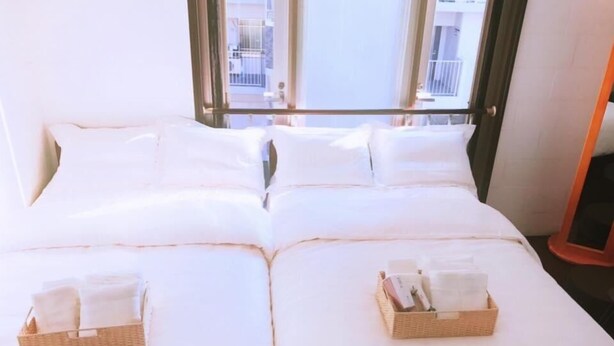A double bed with white linens and two baskets of folded towels. - Osaka Sinsei Guest House (Osaka)