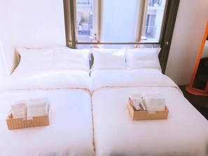 A double bed with white linens and two baskets of folded towels. - Osaka Sinsei Guest House (Osaka)