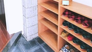 A corner shelving unit with multiple shelves, some of which are filled with shoes. - Osaka Sinsei Guest House (Osaka)