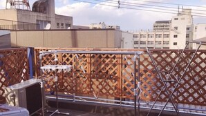A rooftop terrace with a wooden lattice fence, a metal table, and a satellite dish. - Osaka Sinsei Guest House (Osaka)