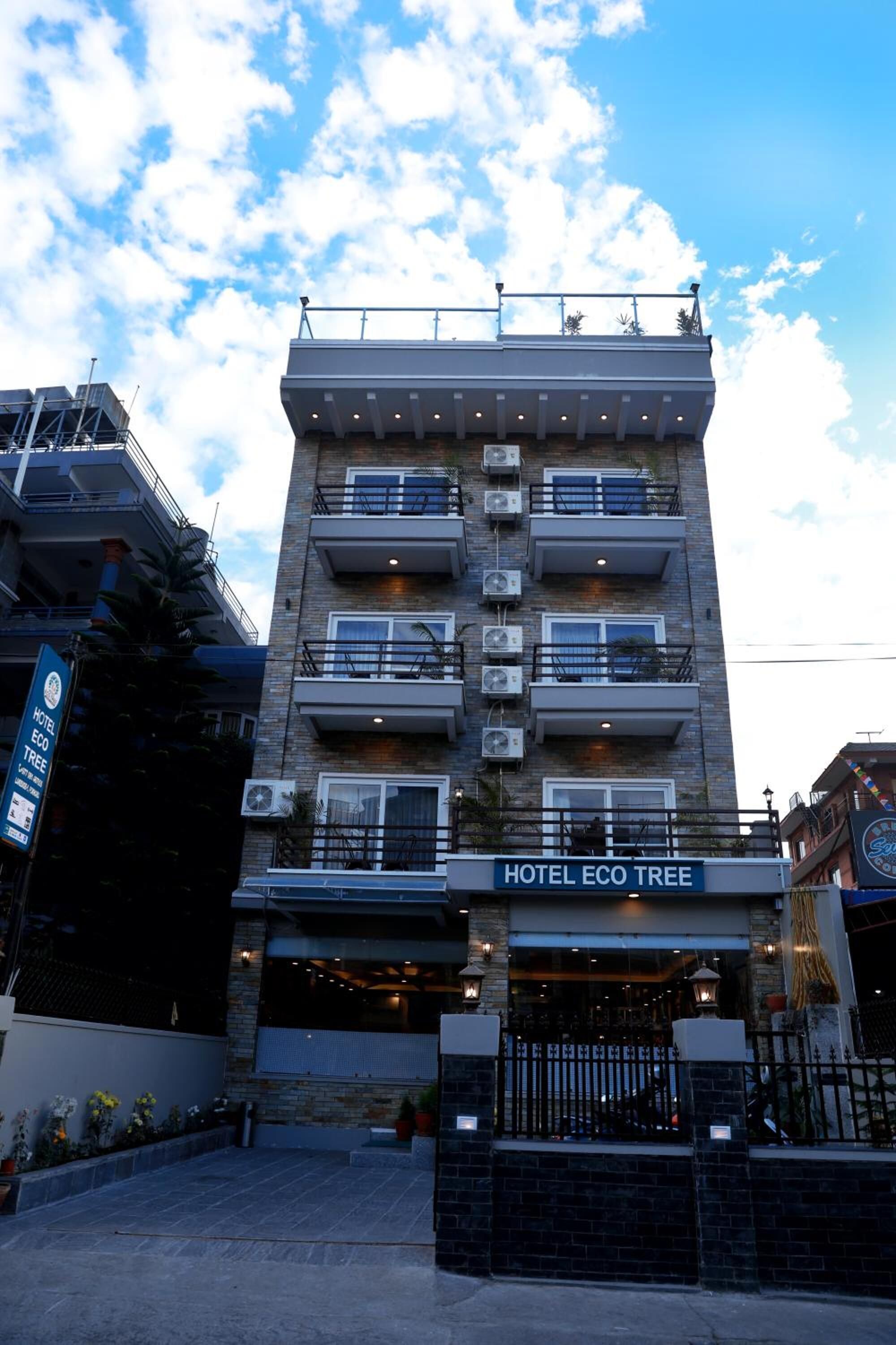 Un hotel de varios pisos llamado "Hotel Eco Tree" con balcones, unidades de aire acondicionado y una entrada bien iluminada.