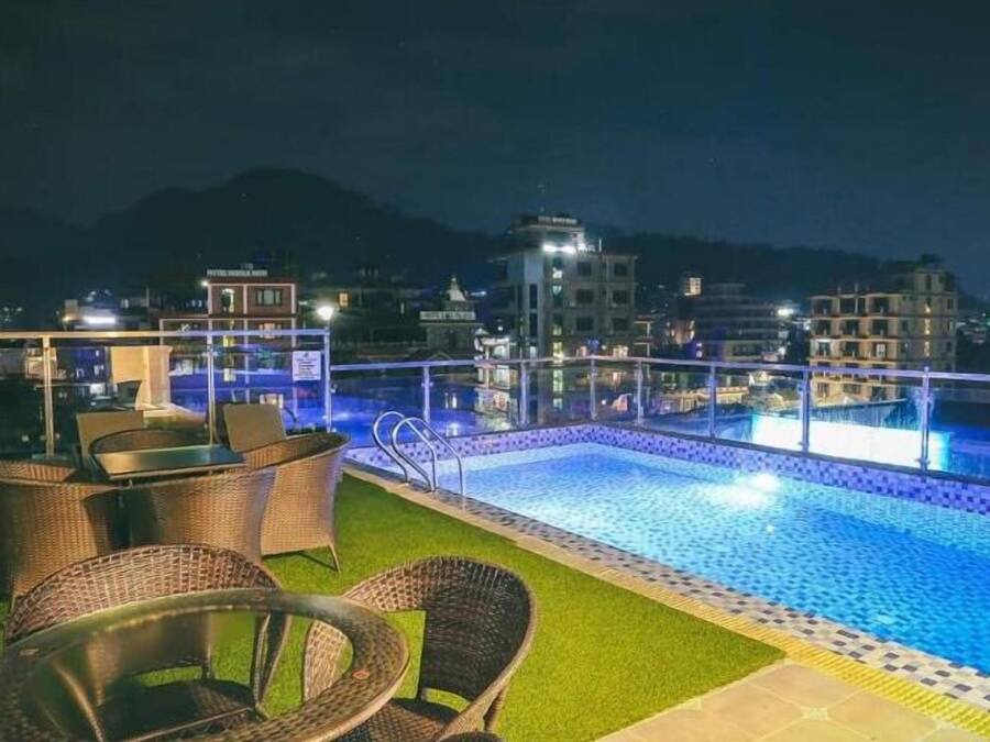 Een zwembad op het dak met rieten stoelen en een glazen balustrade.