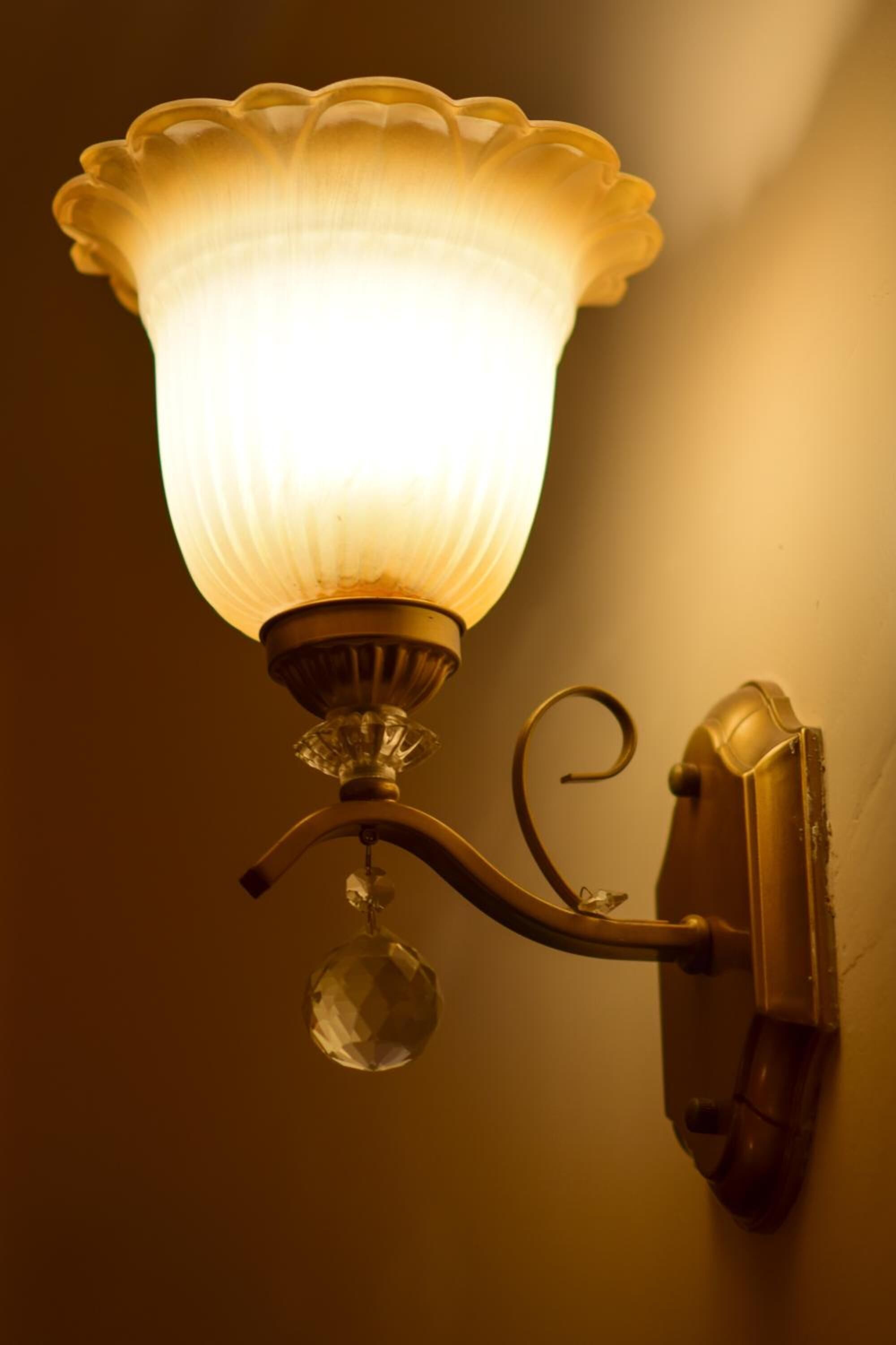 Una lámpara de pared con pantalla de cristal y un adorno de cristal.