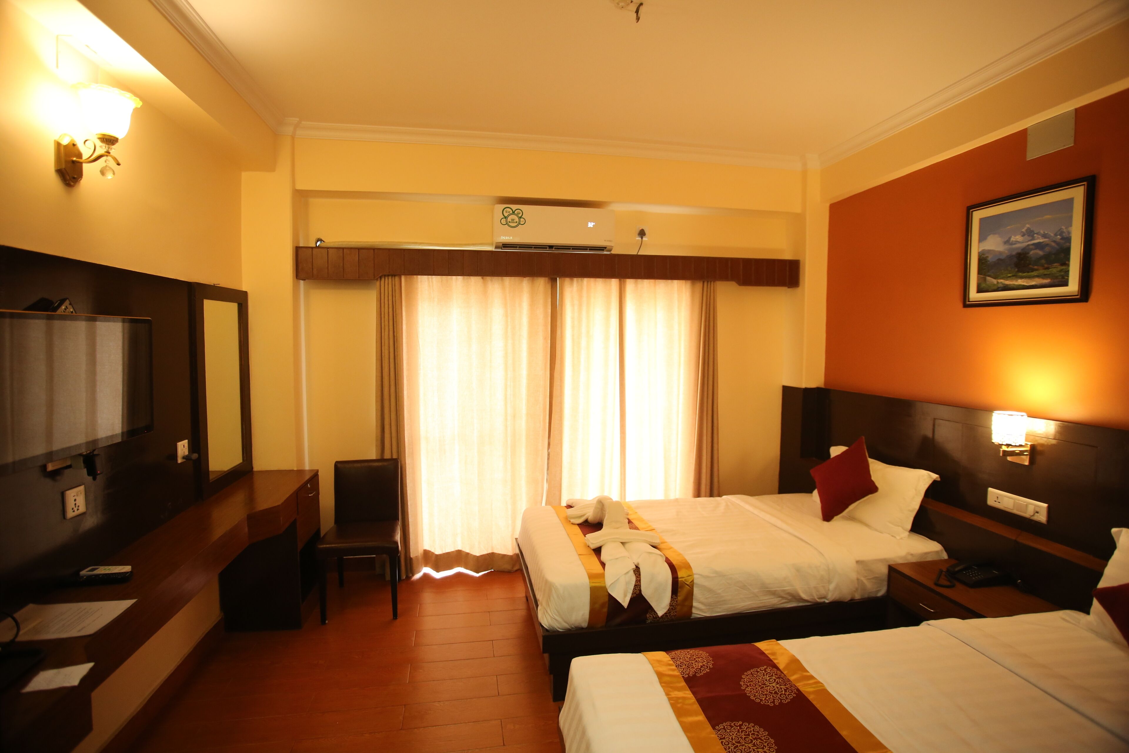 A hotel room with two beds, a desk, a chair, a TV, and an air conditioning unit.