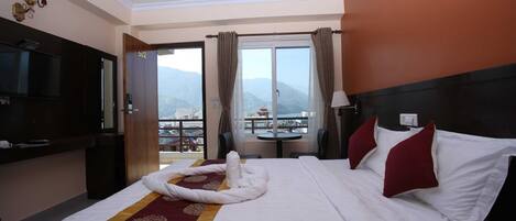 A hotel room with a bed, a TV, a balcony with a view, and a table with a chair.
