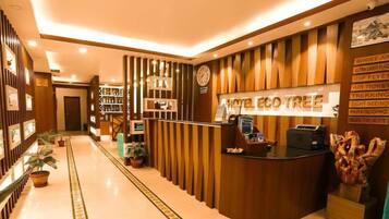 Un espace d’accueil d’hôtel avec un comptoir de réception en bois, une horloge et un panneau indiquant les activités proposées, comme le saut à l’élastique et les randonnées.