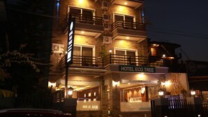 Un hotel de varios pisos con balcones, un letrero que dice "HOTEL ECO TREE" y un coche rojo estacionado adelante.