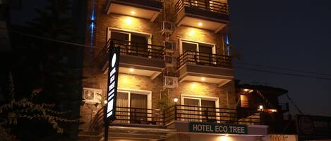 A multi-story hotel with balconies, a sign reading "HOTEL ECO TREE," and a red car parked in front.