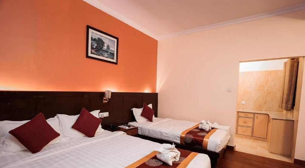A hotel room with two beds, a nightstand, a mirror, and a small kitchenette.