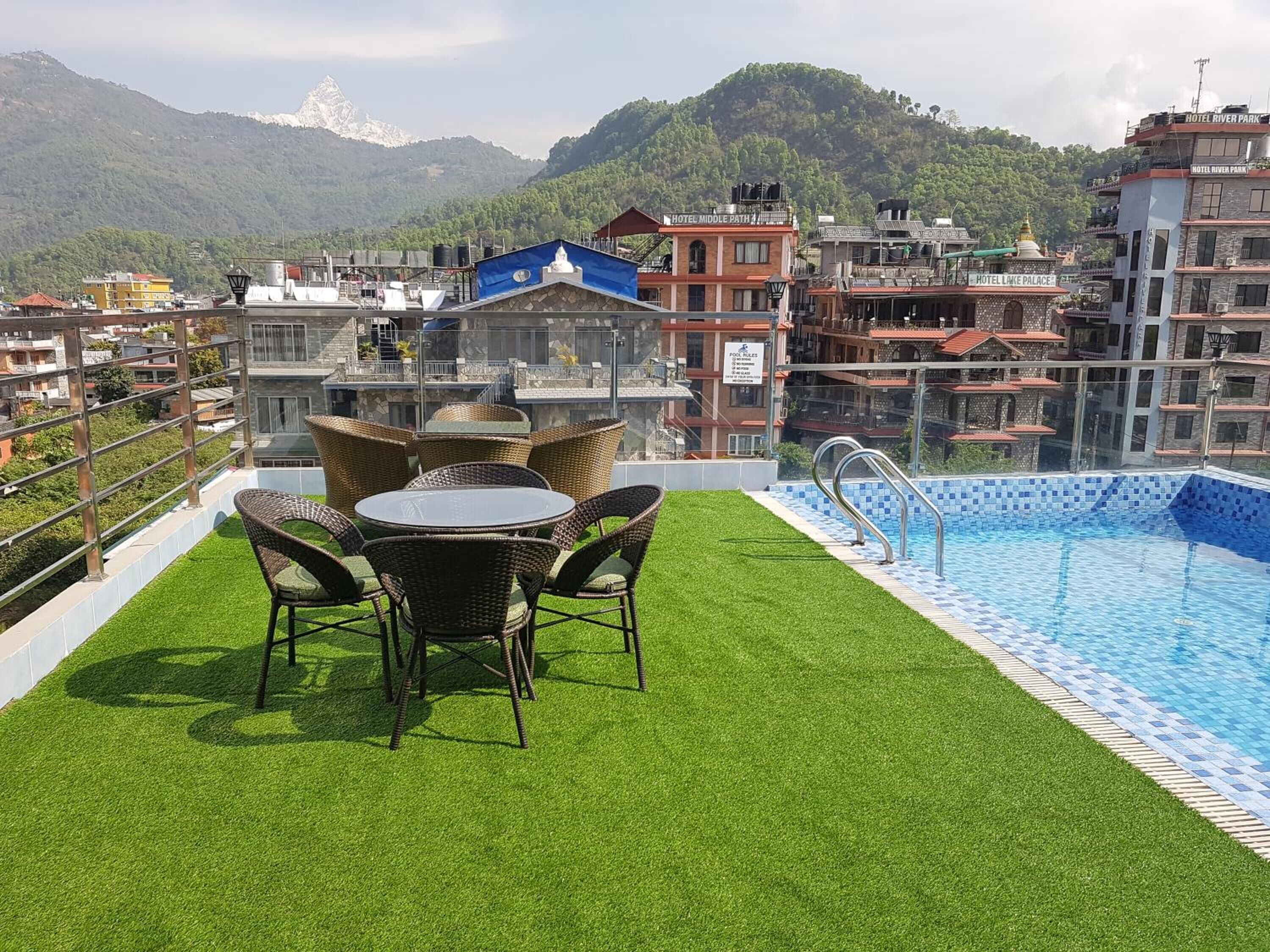 A rooftop pool with artificial grass and wicker furniture, surrounded by hotel buildings with visible signage.