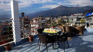 Una terraza con mobiliario de mimbre, una mesa dispuesta con platos y vasos, y una vista de montañas al fondo.