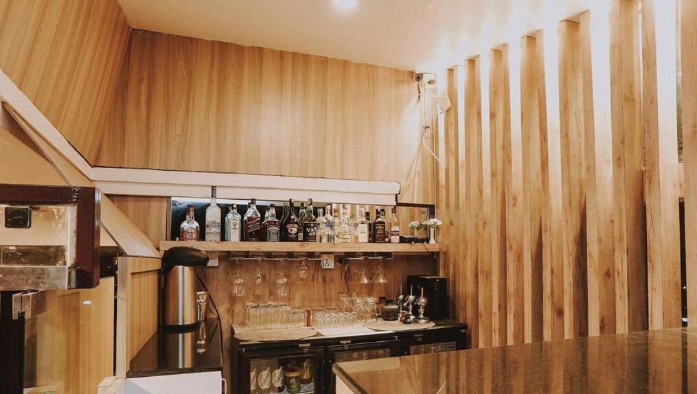 A kitchen with wooden cabinets, a bar area with bottles and glasses, and a stainless steel sink.