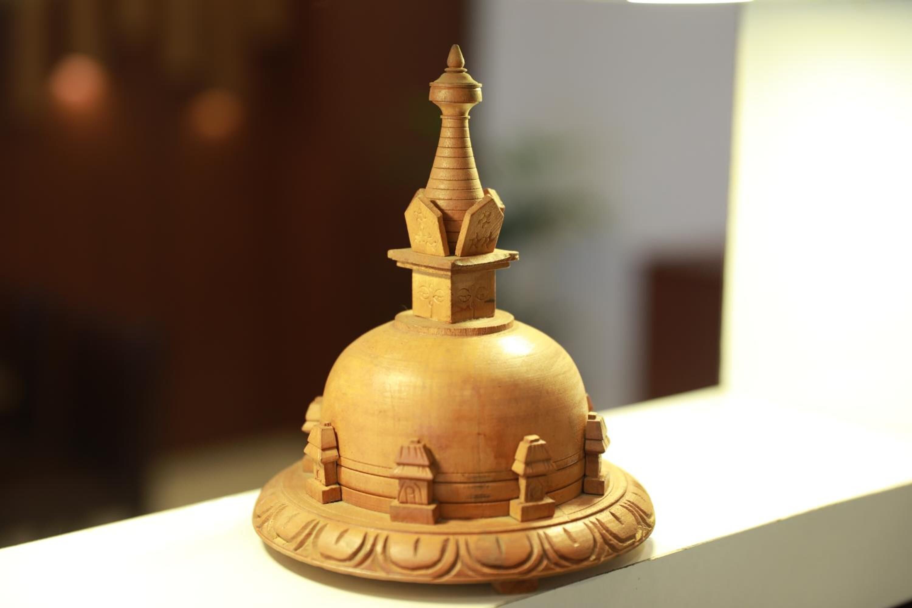 A wooden stupa with a spire, surrounded by smaller structures, displayed on a white surface.