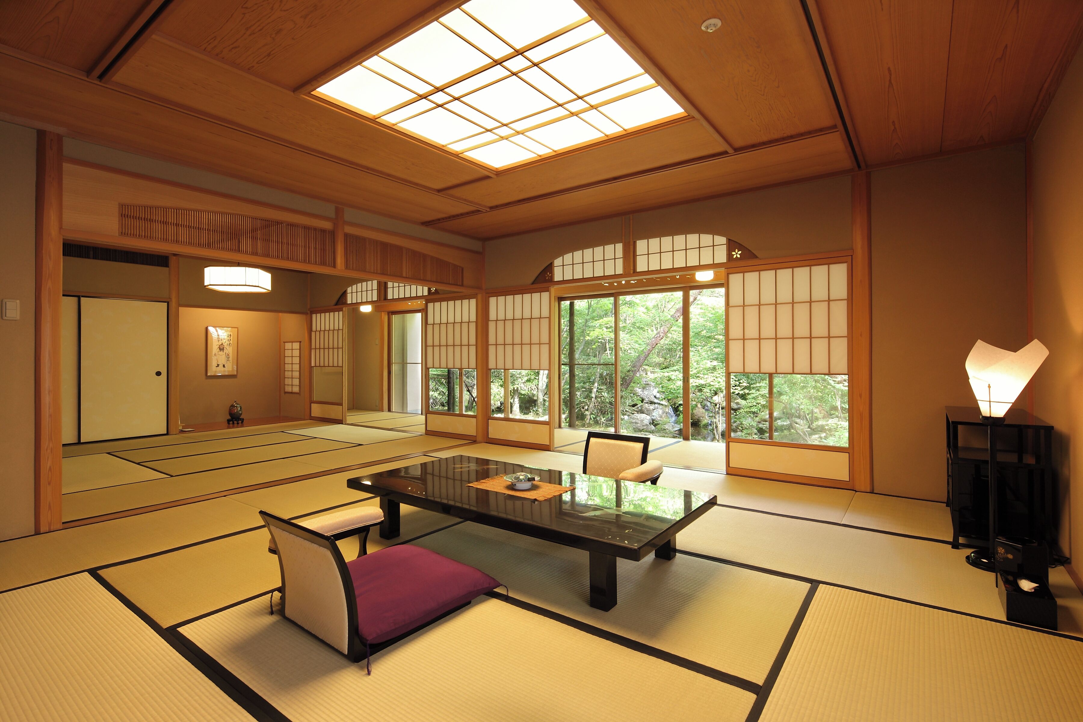 Une pièce de style japonais traditionnel, avec un sol recouvert de tatamis, une table basse, un banc rembourré, des portes coulissantes et une grande fenêtre.