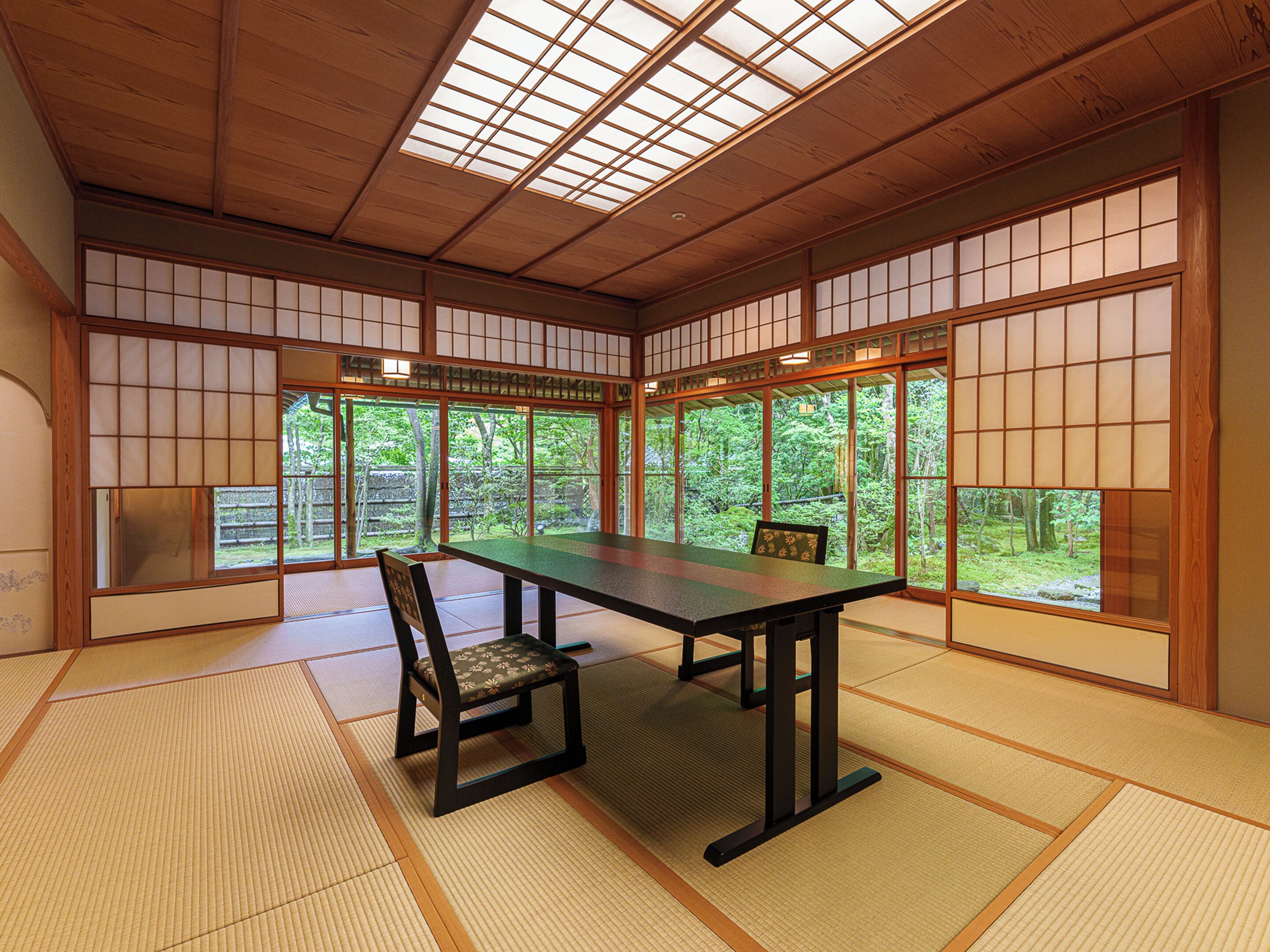 A traditional Japanese room with tatami flooring, a low table, and sliding doors with a view of a forest.