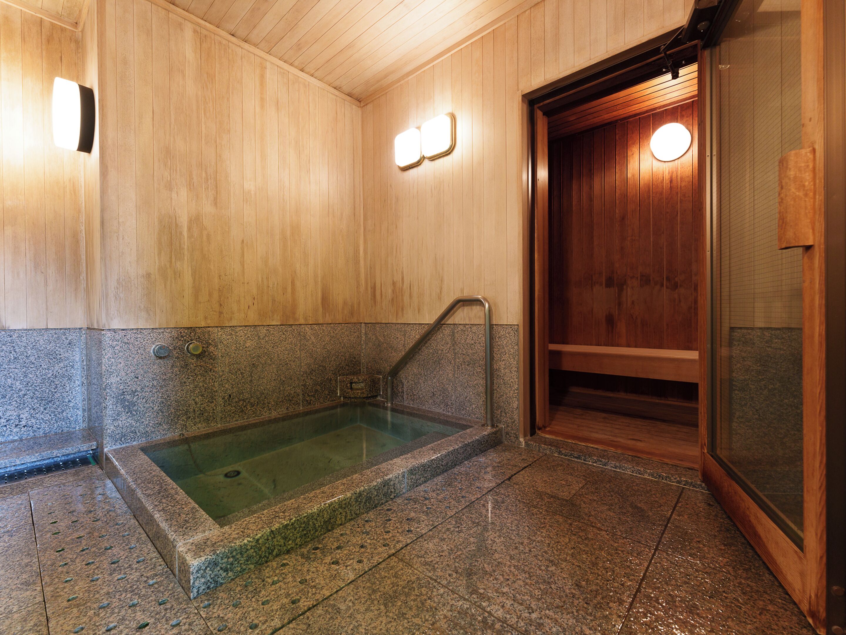 A wooden interior with a stone-floored hot tub area, wooden walls, and a door with a glass panel.