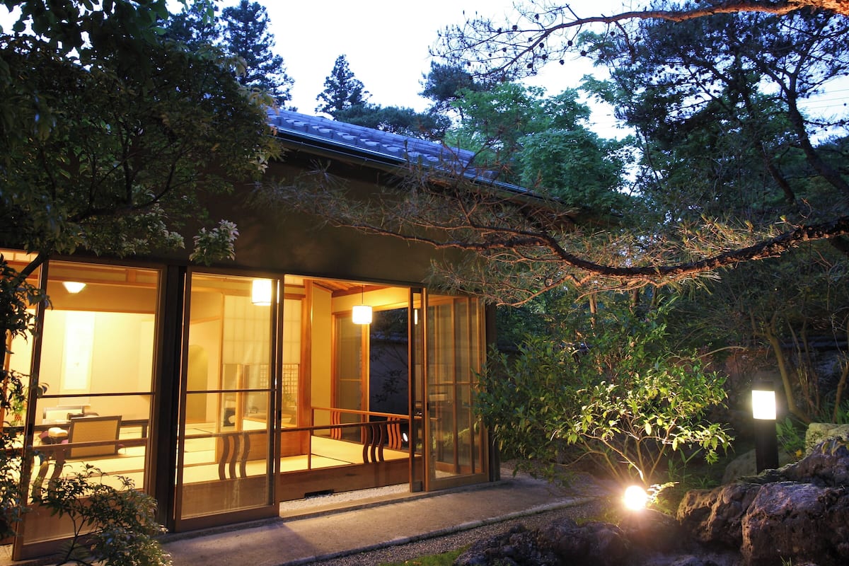 A traditional Japanese-style building with sliding glass doors, a wooden deck, and a stone pathway.