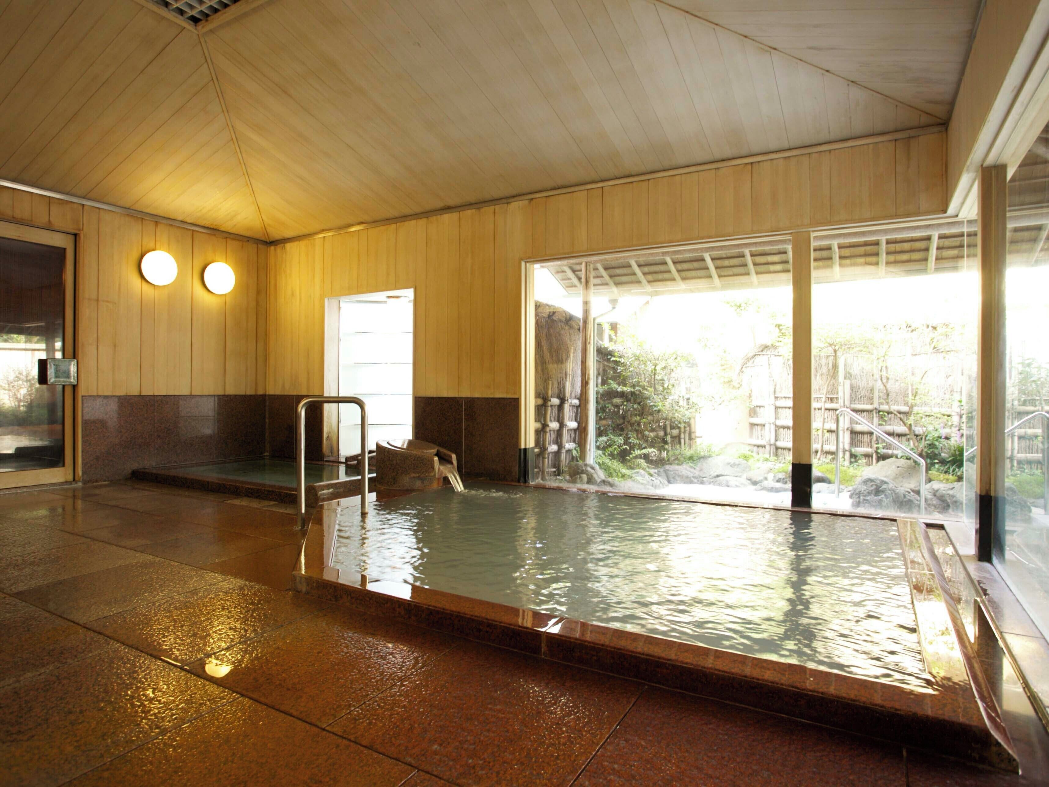 A large indoor swimming pool with a wooden interior, a glass wall, and a view of an outdoor area.