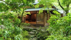 Un edificio tradicional japonés con fachada de madera, un porche cubierto y vistas a un jardín con rocas y vegetación.