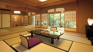 Una habitación japonesa tradicional con suelo de tatami, una mesa baja, un banco acolchado, puertas correderas y ventanas grandes.