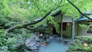 Un edificio tradicional japonés con un estanque de carpas, rodeado de abundante vegetación y rocas.