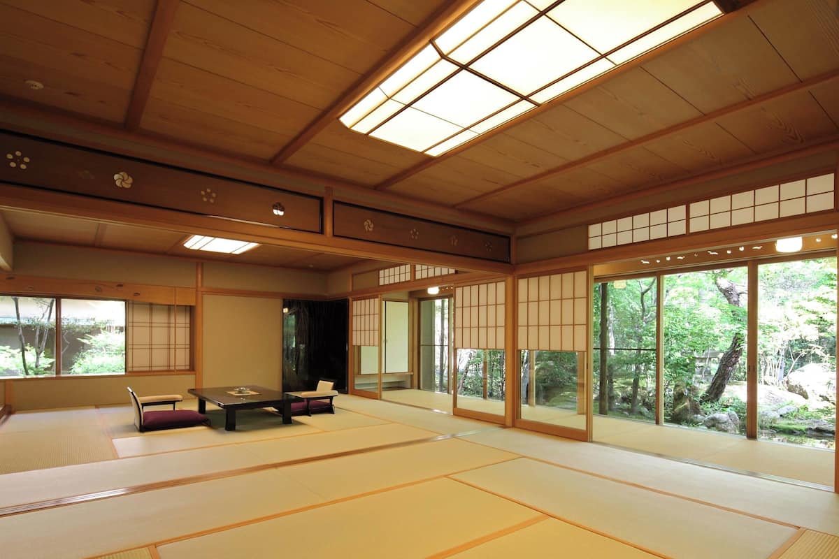 A traditional Japanese room with tatami flooring, sliding doors, and a view of a forest.