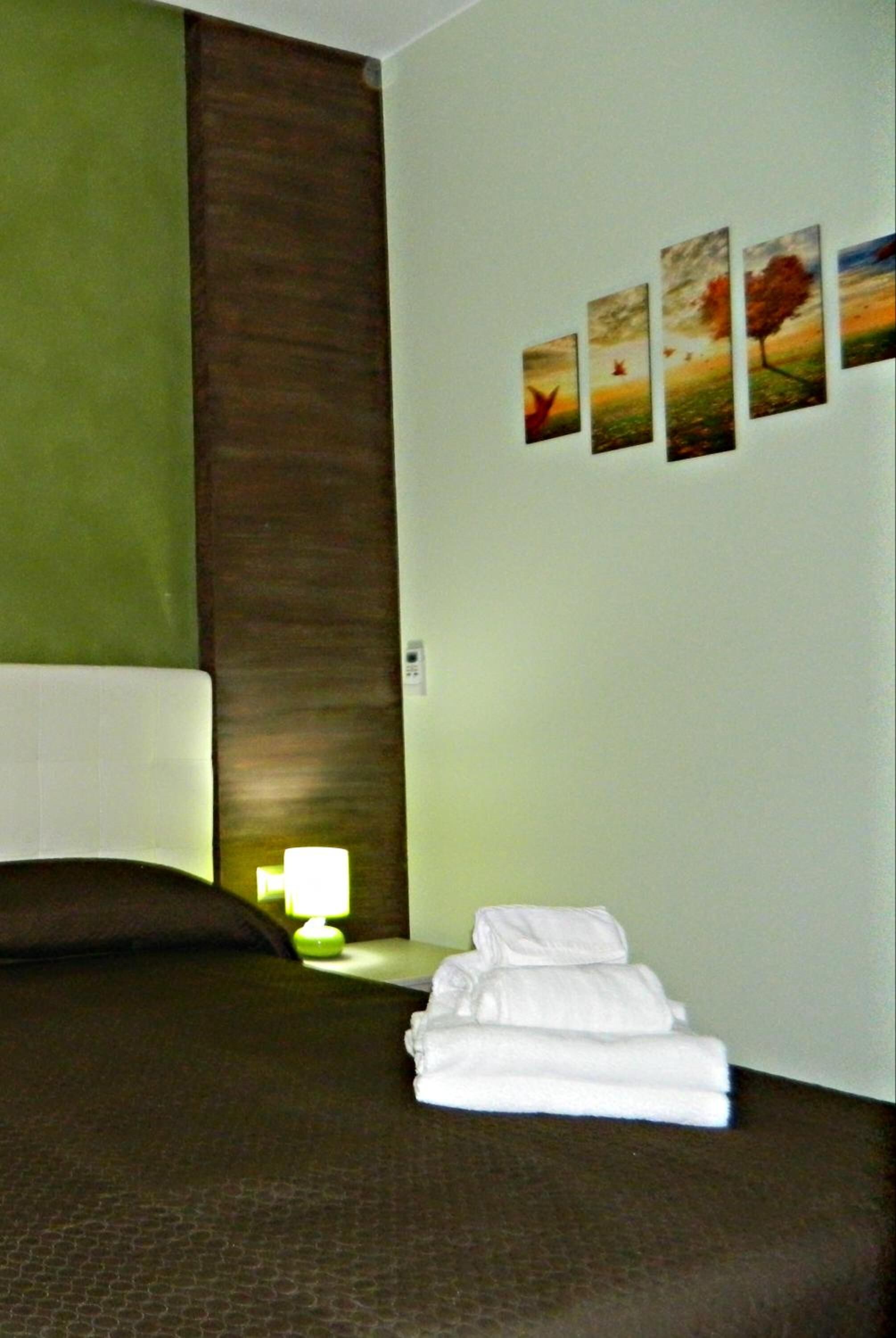 A hotel room with a bed, a nightstand with a lamp, and a wall with four framed pictures.