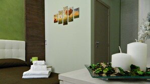 A hotel room with a bed, a bedside table with a tray of flowers, a mirror, and a wall with a series of framed pictures. - Il Borghese Tourist House (Gela)