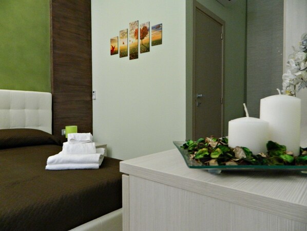 Una habitación de hotel con una cama, una mesita de noche con un florero y un espejo, además de una pared decorada con varios cuadros.
