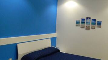 Un dormitorio con una cama, una mesita de noche, una lámpara y una pared decorada con cuatro cuadros.