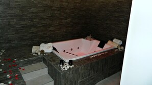 A modern spa with a large freestanding bathtub, dark stone walls, and a ceiling with red lights. - Il Borghese Tourist House (Gela)