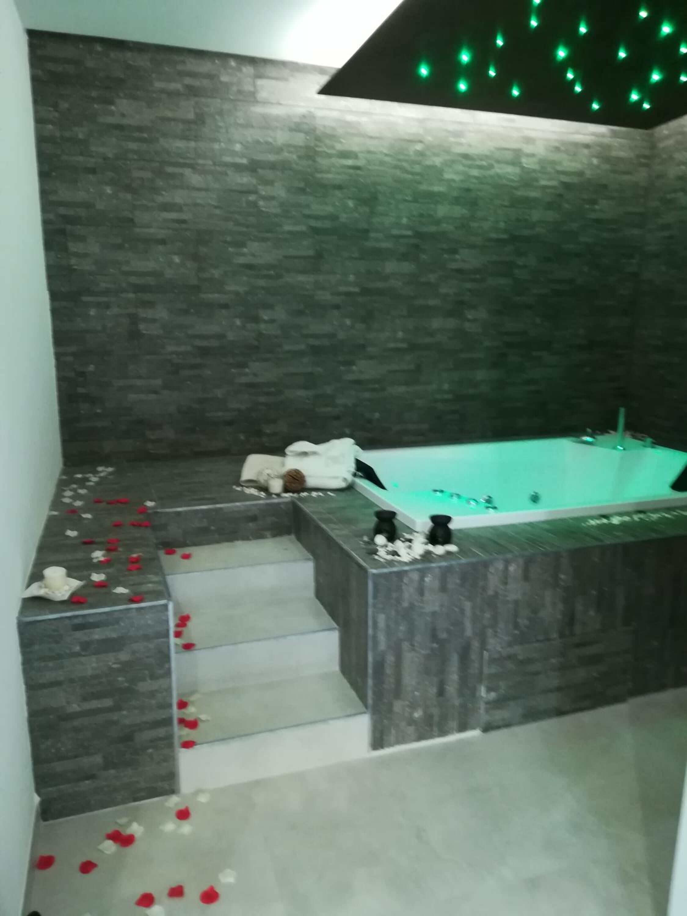 Un baño moderno con una bañera grande, un revestimiento de pared con textura de piedra y una escalera que lleva a la zona de la ducha.