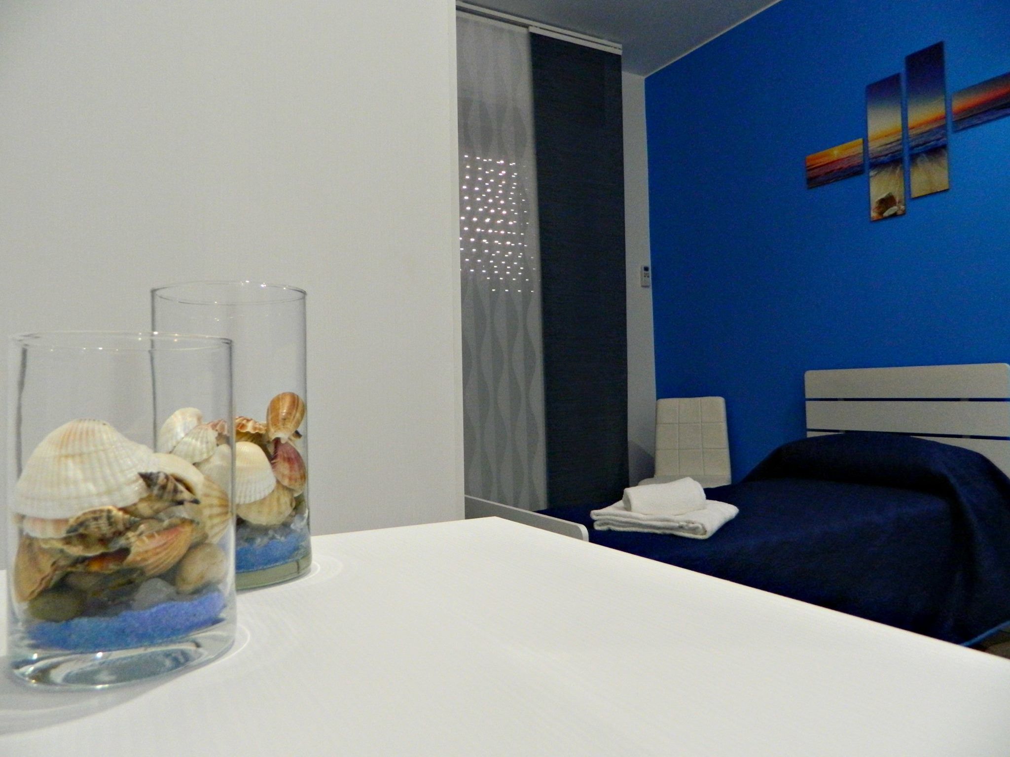 A hotel room with a bed, a nightstand, and two clear vases with seashells on the table.