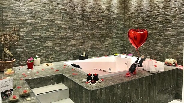 A modern bathroom with a stone wall, a bathtub, and a heart-shaped balloon. - Il Borghese Tourist House (Gela)