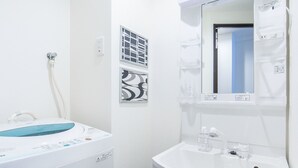 Un baño pequeño con un lavabo blanco, un espejo encima y una lavadora a la izquierda.