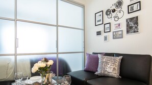 Una sala de estar moderna con una mesa de centro de vidrio, un sofá de cuero negro y un ventanal grande.