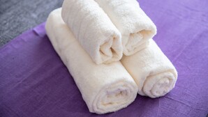 Tres toallas blancas enrolladas sobre una tela morada.