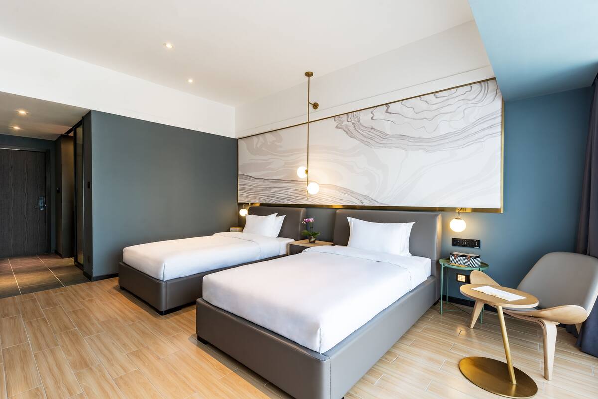 A modern hotel room with two beds, a small table, and a chair.