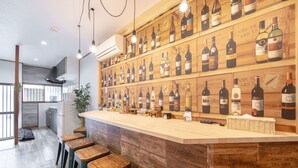A bar area with wooden stools and a wall of wine bottles. - Bar Hostel Shikanzima (Osaka)